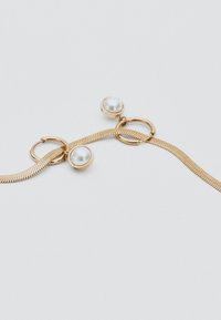 Collana in oro con due grandi charme a perla rotonda attaccati a maglie circolari d'oro su uno sfondo bianco.