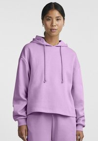 Felpa con cappuccio viola dal taglio largo, con cordini regolabili e polsini a coste, abbinata a pantaloni coordinati in un tessuto morbido e liscio.