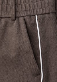 Brown textured fabric with a mesh pattern, featuring a white piping detail along the side and an elastic waistband with a gathered finish.