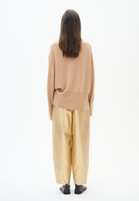 Beige knit sweater with a loose fit, paired with wide-legged light gold trousers and black flat shoes, viewed from the back.