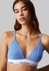 Svijetloplavi trokutasti bralet s tankim trakama i bijelom trakom na kojoj je brendirano 'Calvin Klein'. Mekani, rastezljivi materijal.