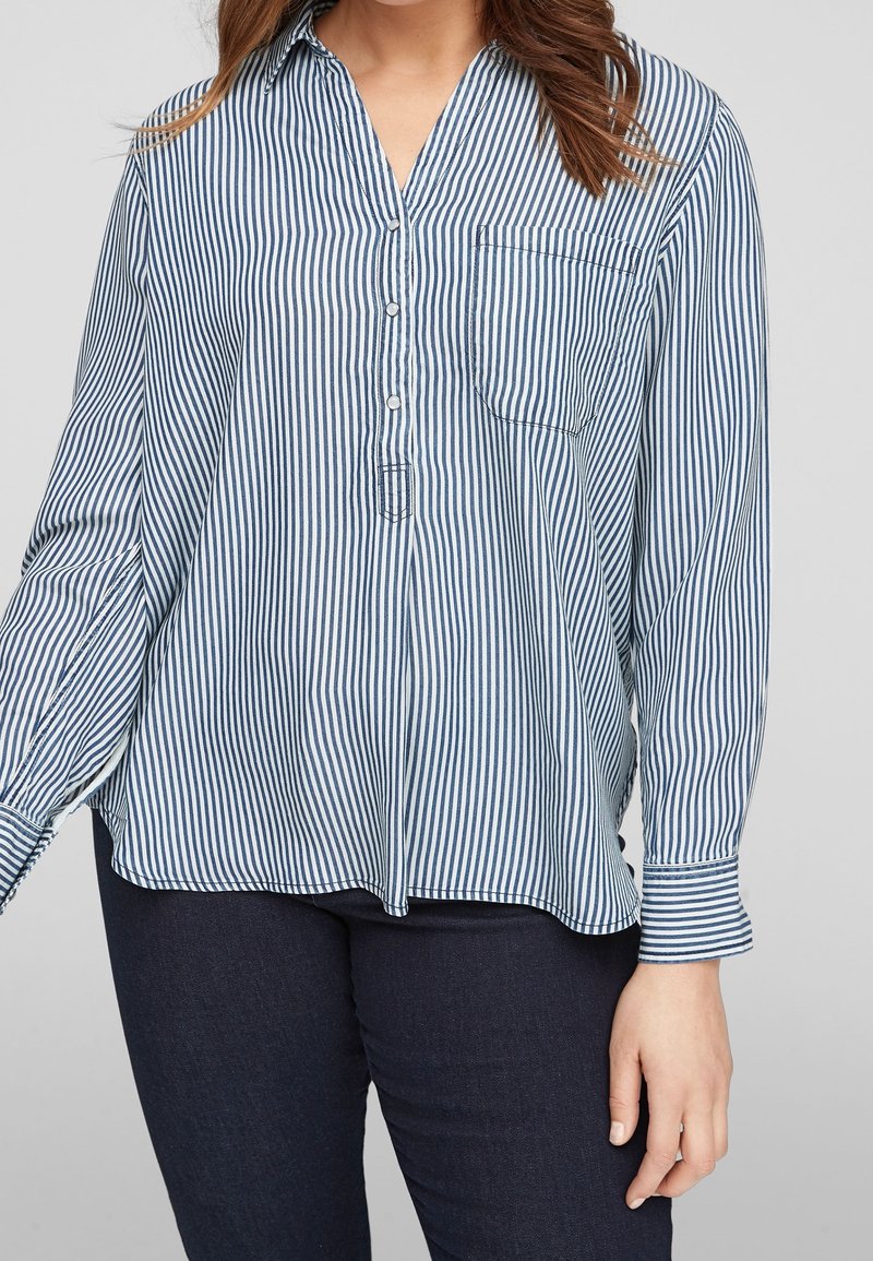 Camicia abbottonata a righe verticali blu e bianche, dotata di colletto, maniche lunghe e taschino sul petto, realizzata in tessuto leggero.