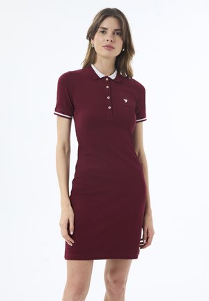 Burgundské polo šaty s krátkým rukávem, bílým límcem a kontrastními pruhy na rukávech. Obsahují tři knoflíky a malé logo na hrudi.