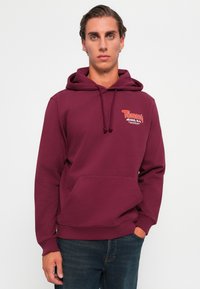 Bordeaux hætte sweatshirt lavet af bomuldsblanding, med en front kangaroo lomme og et logo på brystet i kontrastfarver.