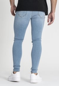 Jeans skinny azul claro con una textura suave, diseño de cinco bolsillos y detalles de costura sutiles, combinados con zapatillas blancas.