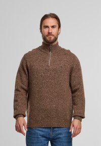 Brauner Strickpullover mit hohem Kragen und halbem Reißverschluss. Mit helleren Farbflecken strukturiert und mit gerippten Bündchen und Saum versehen.