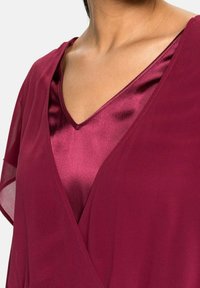 Haut bordeaux avec un design en V, en satin et en chiffon, superposé pour un effet texturé, avec des manches fluides.