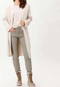 Beżowy długi kardigan, lekka bluzka, zielone slim fit spodnie i beżowe botki z futerkiem. Miękkie tekstury, prosty design i neutralna paleta kolorów.