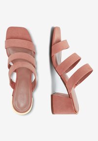 Sandales à talon bloc en suède rose avec trois larges lanières à travers le pied, présentant une semelle intérieure lisse et un accent métallique sur le talon.