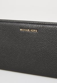 Black textured leather wallet with a gold "MICHAEL KORS" logo. The surface features a grainy pattern, enhancing its tactile quality.