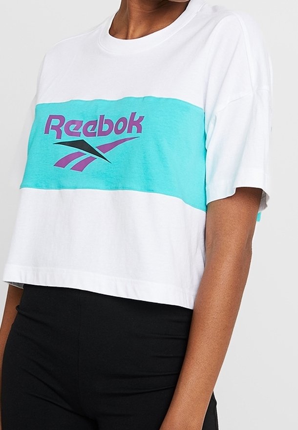 Zkrácená bílá tričko s tyrkysovým a fialovým logem Reebok; má design s barevnými bloky a jemnou bavlněnou strukturu. Krátké rukávy.