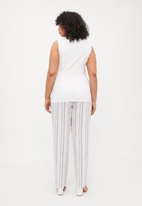 Top blanco sin mangas combinado con pantalones sueltos de rayas en colores claros. Los pantalones presentan rayas azules verticales y un ajuste relajado.