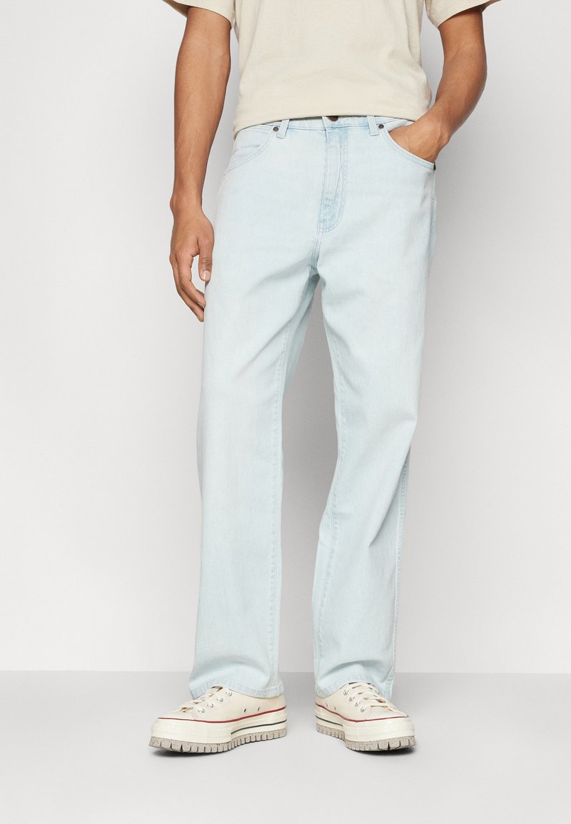 Heledsinine denim püksid otse jala lõikega, klassikalise viie taskuga disainiga ja kantud beežide kangast tennisetega.