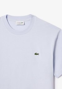 Lys blå t-skjorte i bomull med en klassisk passform, med en liten grønn brodert krokodillelogo på venstre bryst. Rund hals.