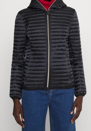 Schwarze, gesteppte Jacke mit Reißverschluss und Kapuze, getragen über einem roten Rollkragenpullover und kombiniert mit blauen Jeans.