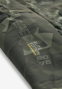 Tkanina s camo vzorom v tmavozelenej farbe s textúrovaným povrchom. Obsahuje nápis "SPEC ELITE EDITION" a výkonové detaily vytlačené v šedej a žltej farbe.