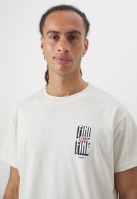 Cremfarbendes Baumwoll-T-Shirt mit einem Frontprint, der in schwarzem und pinkem Text "FIND ALLA FINE" und "JUVENTUS" zeigt. Kurze Ärmel, runder Ausschnitt.