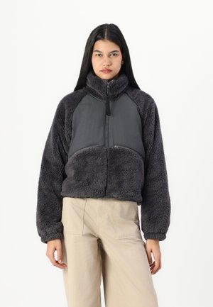 Short, cropped gray fleece jacket with a high collar, front zipper, and contrasting smooth fabric panel at the chest. Features wide sleeves.
