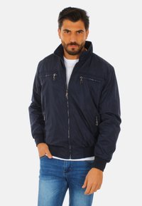 Giacca bomber blu navy realizzata in tessuto leggero, con un colletto alto, tasche con zip e polsini elasticizzati per una vestibilità aderente.
