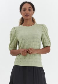 Blusa verde chiaro con texture, maniche corte a palloncino e scollo rotondo, realizzata in tessuto stropicciato. Finitura liscia e vestibilità rilassata.