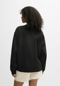 Felpa nera oversize con una vestibilità comoda e scollatura a coste, abbinata a pantaloni corti beige sfrangiati. Tessuto testurizzato, stile informale.