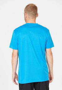 Kortärmad atletisk tröja i ljusblått, tillverkad av fukttransporterande material. Har en rundad halsringning och en slät yta. Bakvy visas.