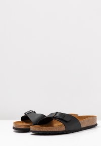 Sorte slide-sandaler med en korkfodersål. Har en bred strap med en justerbar spænde og en tekstureret gummisål for bedre greb.
