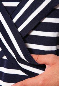 Marineblau- und weiß gestrefter Stoff mit einem Überkreuzdesign. Das Material hat eine glatte Textur, wobei eine Hand den Stoff für Details hält.