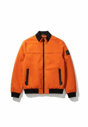 Veste aviateur orange avec col, poignets et ceinture noirs, poches verticales zippées et fermeture éclair frontale, présentée à plat sur fond blanc.