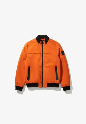 Veste aviateur orange avec col, poignets et ceinture noirs, poches verticales zippées et fermeture éclair frontale, présentée à plat sur fond blanc.