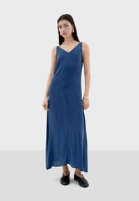 Blauwe mouwloze maxi jurk met een v-hals, met een soepele textuur en een rechte silhouette, gecombineerd met zwarte instap schoenen.