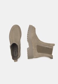 Beige ankle boots made of suede, featuring elastic side panels, textured rubber sole, and contrasting stitching detail.