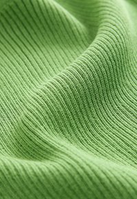 Tissu vert côtelé avec une surface texturée, présentant des rainures parallèles, créant un motif uniforme et une apparence douce.
