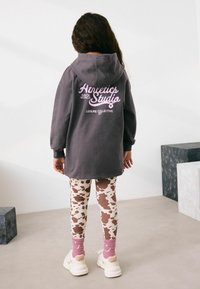 Grå oversized hoodie med pink tekst, mønstrede leggings i creme og brun ko-design, pink sokker og hvide sneakers.