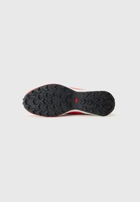 Red and white athletic shoe outsole with a textured black rubber grip, featuring a triangular accent and patterned tread for traction.