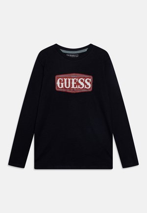 Chemise noire à manches longues avec un logo rectangulaire rouge et blanc portant l'inscription "GUESS" centré sur la poitrine, col rond.
