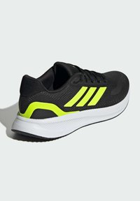 Sorte atletiske sko med mesh-overdel, neongule detaljer, tekstureret sål og tre diagonale striber på siden; designet til komfort og præstation.