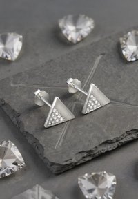 Silver triangulära örhängen med en texturerad sida och små klara stenar, monterade på en solid post med en blomformad bakdel.