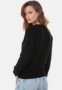 Pull noir avec un col rond, des manches longues et un ourlet côtelé. Présente un tricot texturé et une coupe décontractée, associé à un jean bleu clair.
