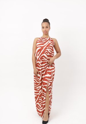 Mujer de pie vistiendo un vestido maxi sin mangas de estampado de cebra naranja y blanco con una abertura lateral y tacones altos negros sobre un fondo blanco liso.