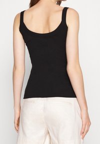 Czarny bawełniany top na ramiączkach z szerokimi paskami i dopasowanym krojem. Gładka faktura, zaokrąglony dekolt i wykończenie na wysokości talii.