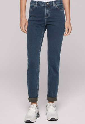 Dunkelblaue Denim-Jeans mit schmaler Passform, ausgestattet mit einem klassischen Fünf-Taschen-Design, sichtbaren Nähten und umgeschlagenen Säumen, kombiniert mit weißen Sneakers.