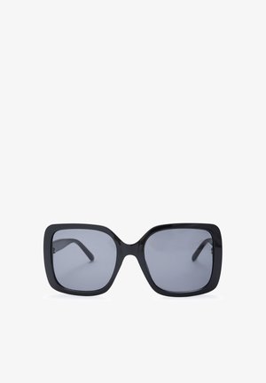 Lunettes de soleil carrées noires oversize avec des verres teintés foncés sur fond blanc.