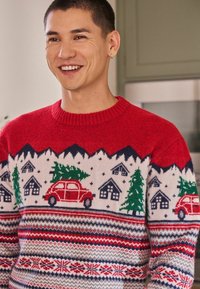 Red knit sweater with festive designs, including red cars, trees, and houses. Features a ribbed crew neck and patterned bands in navy and white.