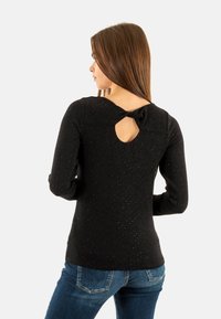 Top nero a maniche lunghe con finitura texturizzata, dotato di dettaglio a chiave sul retro e accentuato da un fiocco. Abbinato a jeans in denim blu.