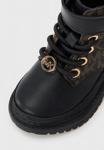 Black leather ankle boot featuring a patterned fabric panel, gold-tone hardware, black laces, and a textured rubber sole.