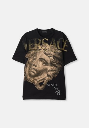 T-shirt en coton noir avec un imprimé graphique doré représentant une tête, un grand texte "VERSACE" et le slogan "TROP N'EST JAMAIS ASSEZ". Manches courtes.