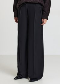 Schwarze weit geschnittene Hose aus glattem Stoff mit vorderen Falten, die eine taillierte Passform und eine weiche, fließende Textur aufweist.