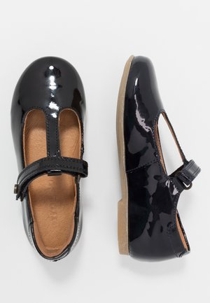 Coppia di scarpe Mary Jane in vernice nera lucida con soletta beige e strap in velcro, viste dall'alto e di lato.