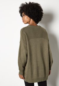 Olive zielony oversize'owy sweter dzianinowy z opadającymi ramionami, prążkowanymi mankietami i dołem, wyróżniający się teksturowanym wykończeniem i luźnym krojem.